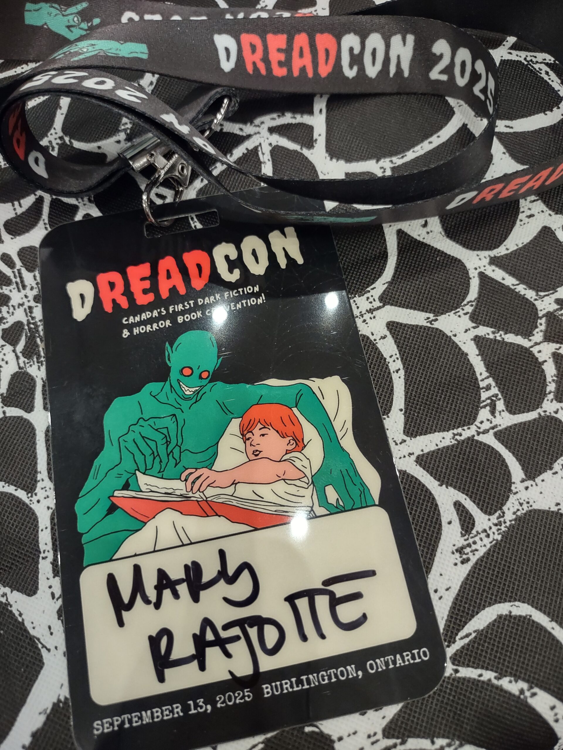 Lanyard for DreadCon with a green creature reading a bedtime story toa child.