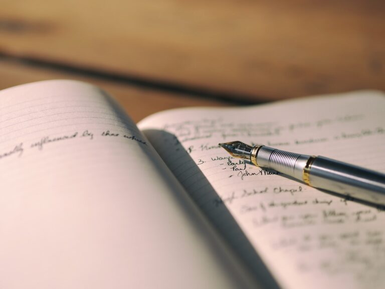 An open composition book with blurry writing and a fountain pen laying on the pages